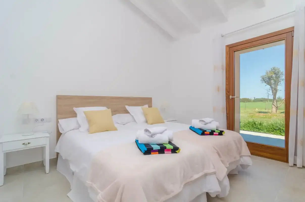 A bright bedroom with a bed, bedside table, and a window overlooking greenery.