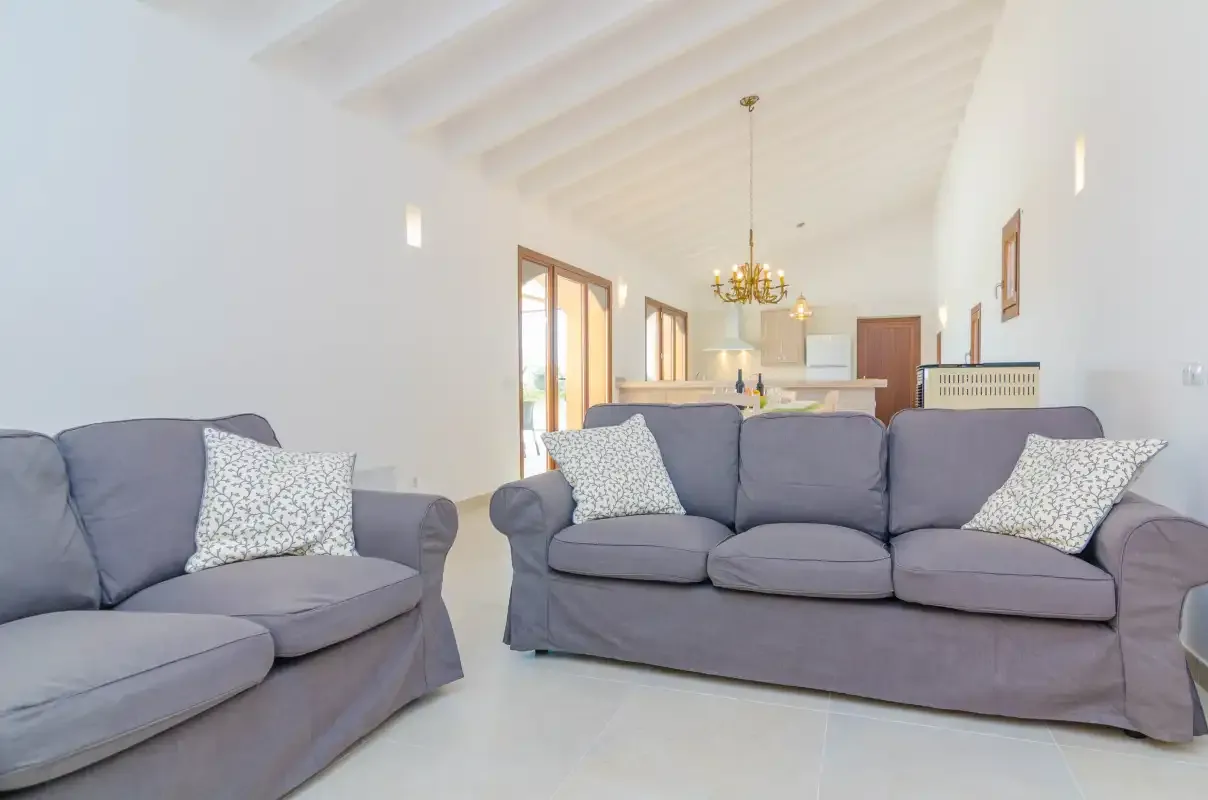 A bright living room with gray seating and an open kitchen in the background.