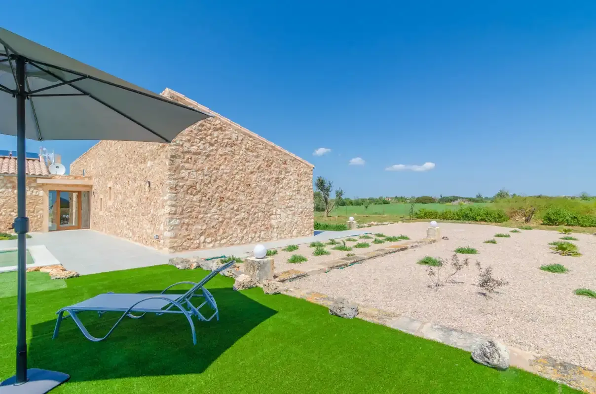 A stone building stands beside a lawn and a sunny gravel courtyard.
