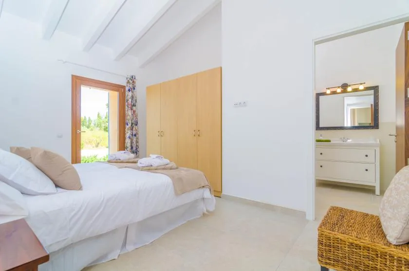 A bright bedroom with a bed, wooden wardrobe, and doorway to a vanity area.