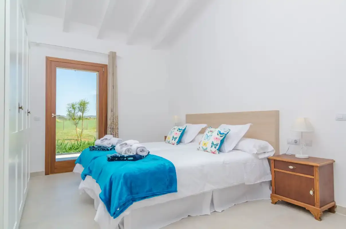 A bright bedroom with a bed dressed in white and a turquoise blanket.