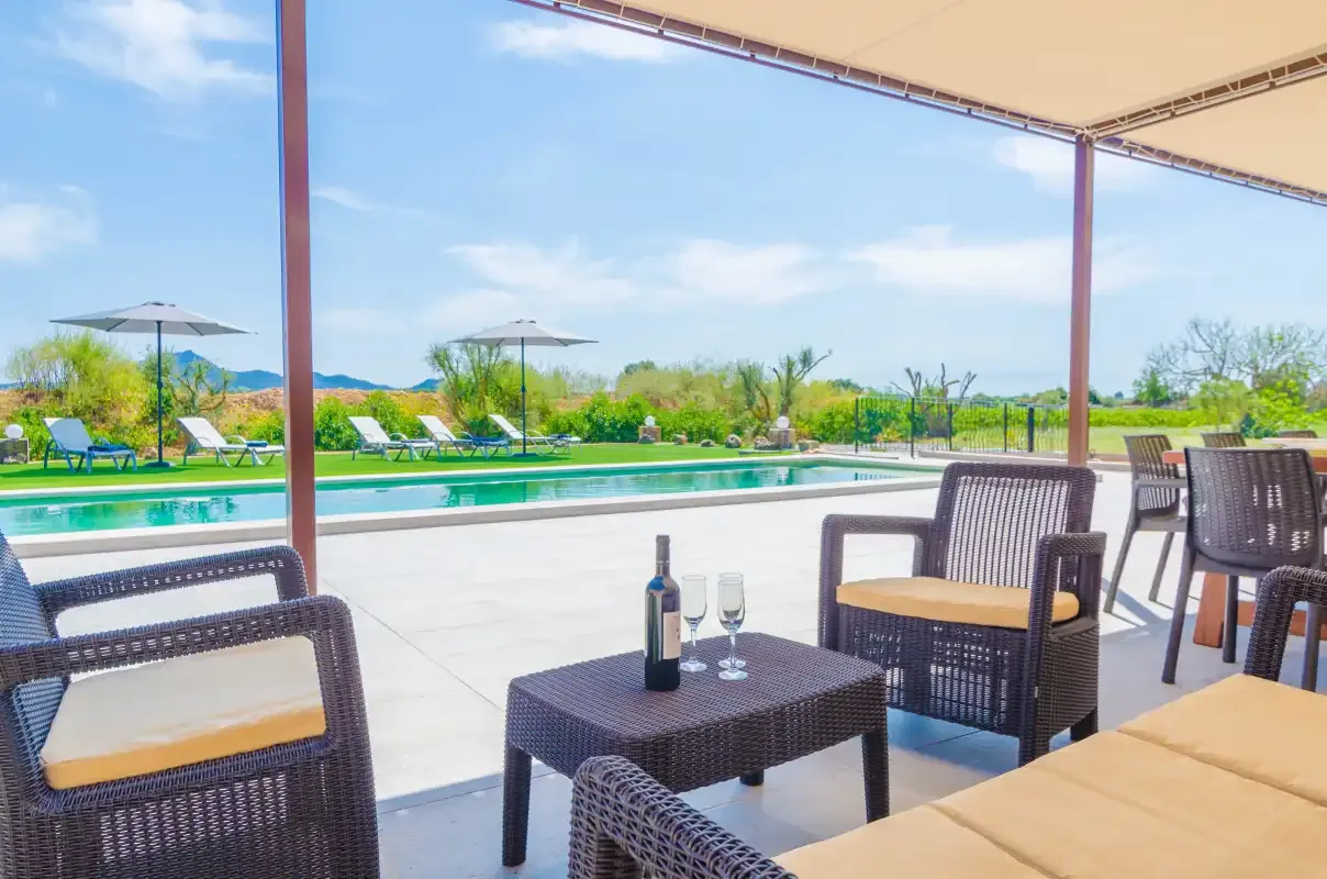 A covered patio with outdoor seating overlooks a swimming pool and garden.
