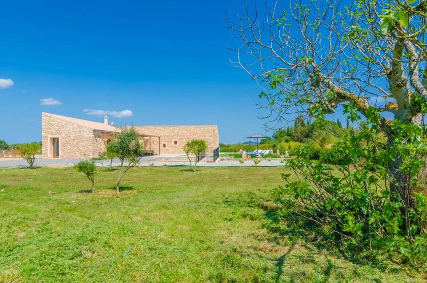 A low stone building stands beyond a grassy lawn under a clear blue sky.