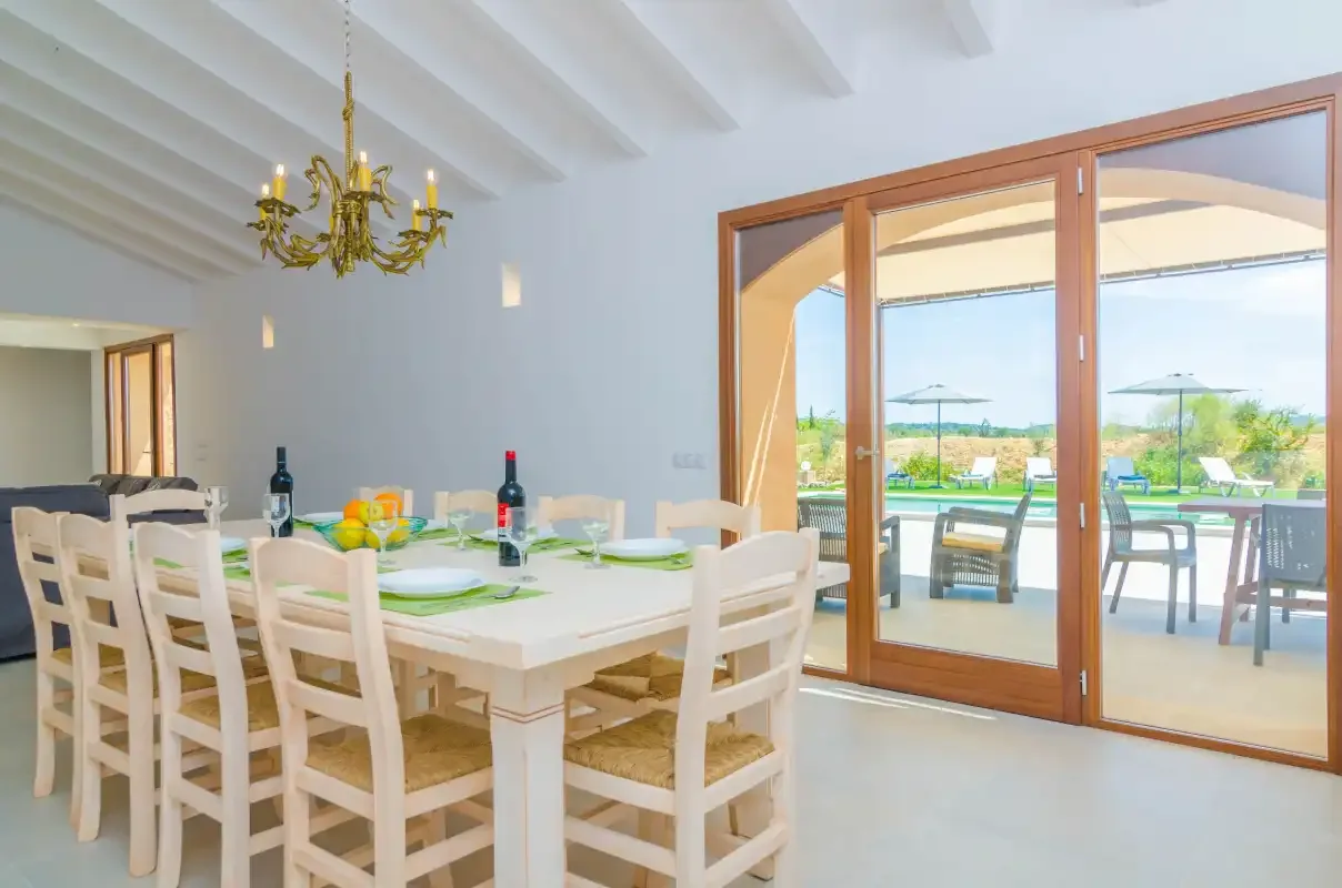 A bright dining area with a long table beside glass doors opening onto a patio.