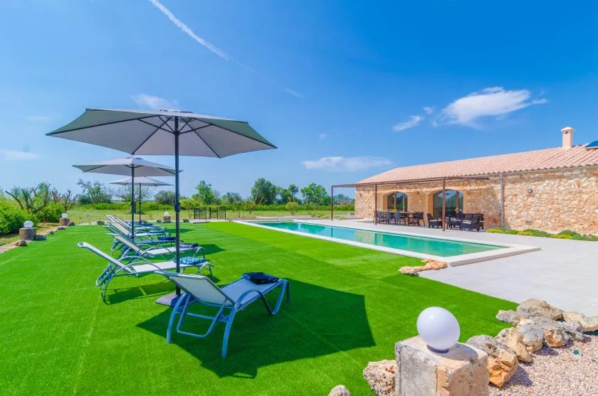 A swimming pool beside a stone building, with sun loungers on the lawn.