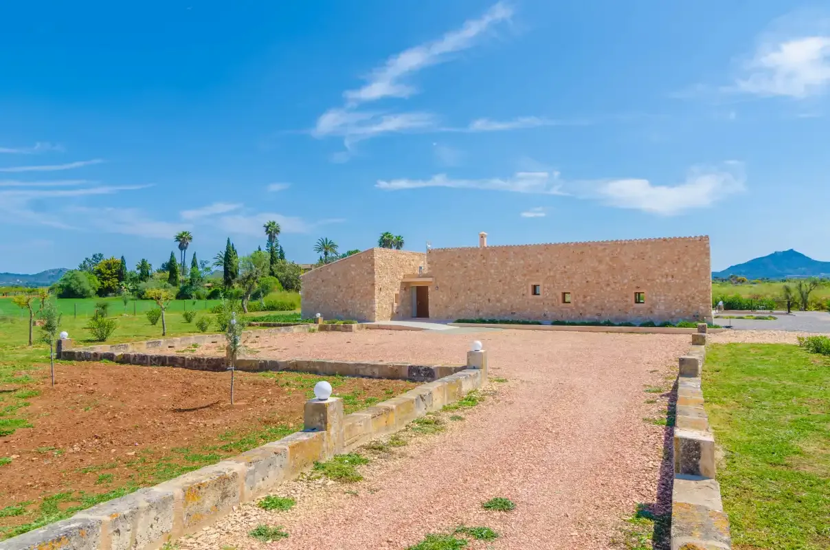 A long stone building stands at the end of a gravel driveway, surrounded by open grounds.