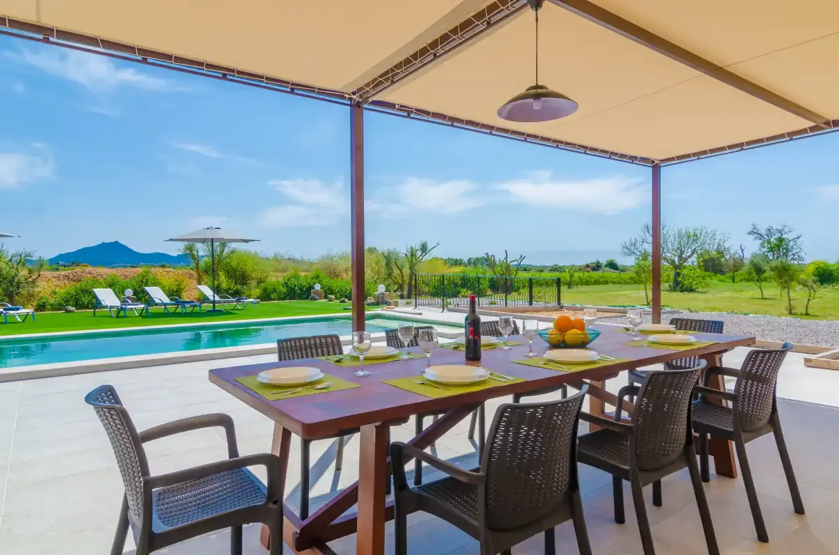 A shaded outdoor dining area overlooks a swimming pool and green fields.