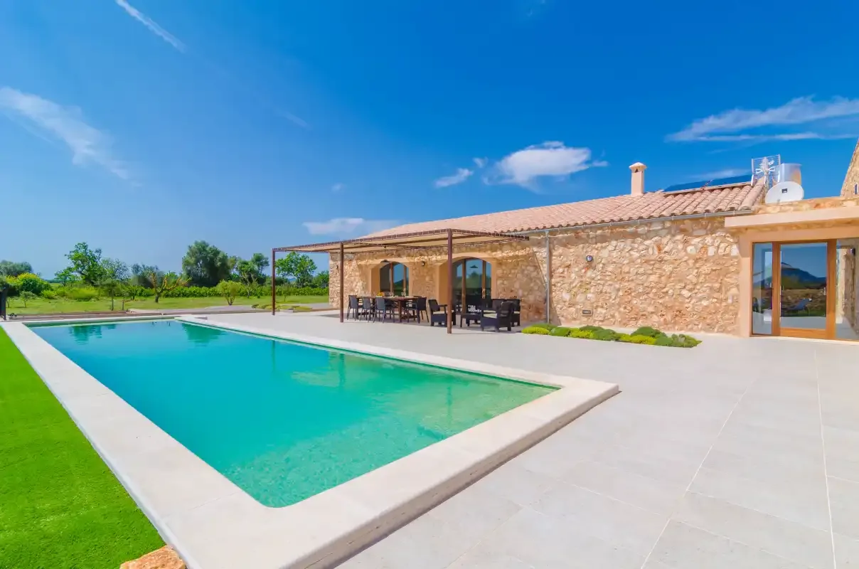 A stone house with a swimming pool and a shaded outdoor seating area.