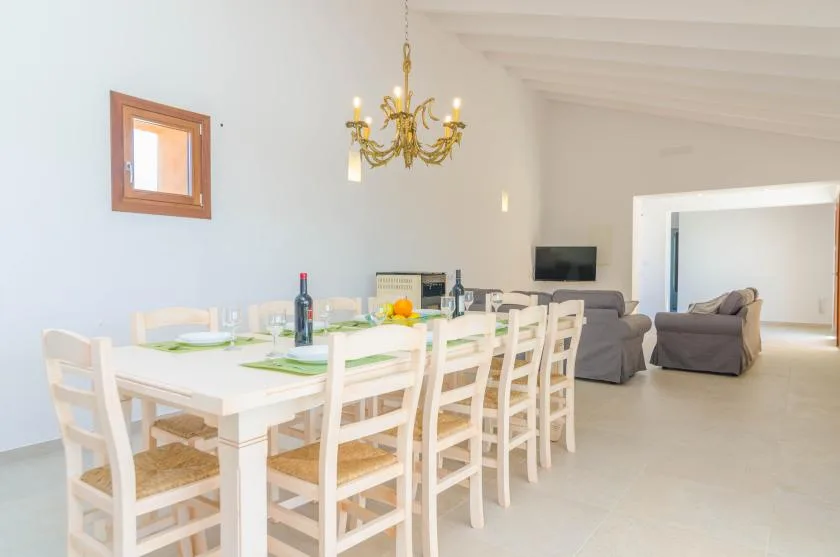 A bright dining area with a long white table and seating beside a living area.
