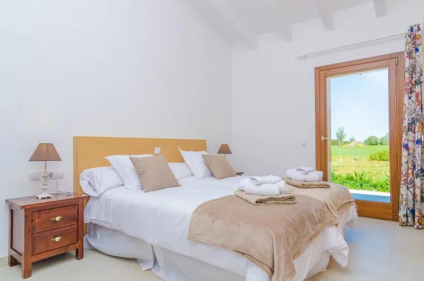 A bright bedroom with a neatly made bed and a large window overlooking greenery.