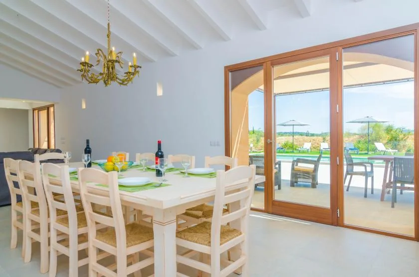 A bright dining room with a long table set beside wide glass doors opening to a patio.