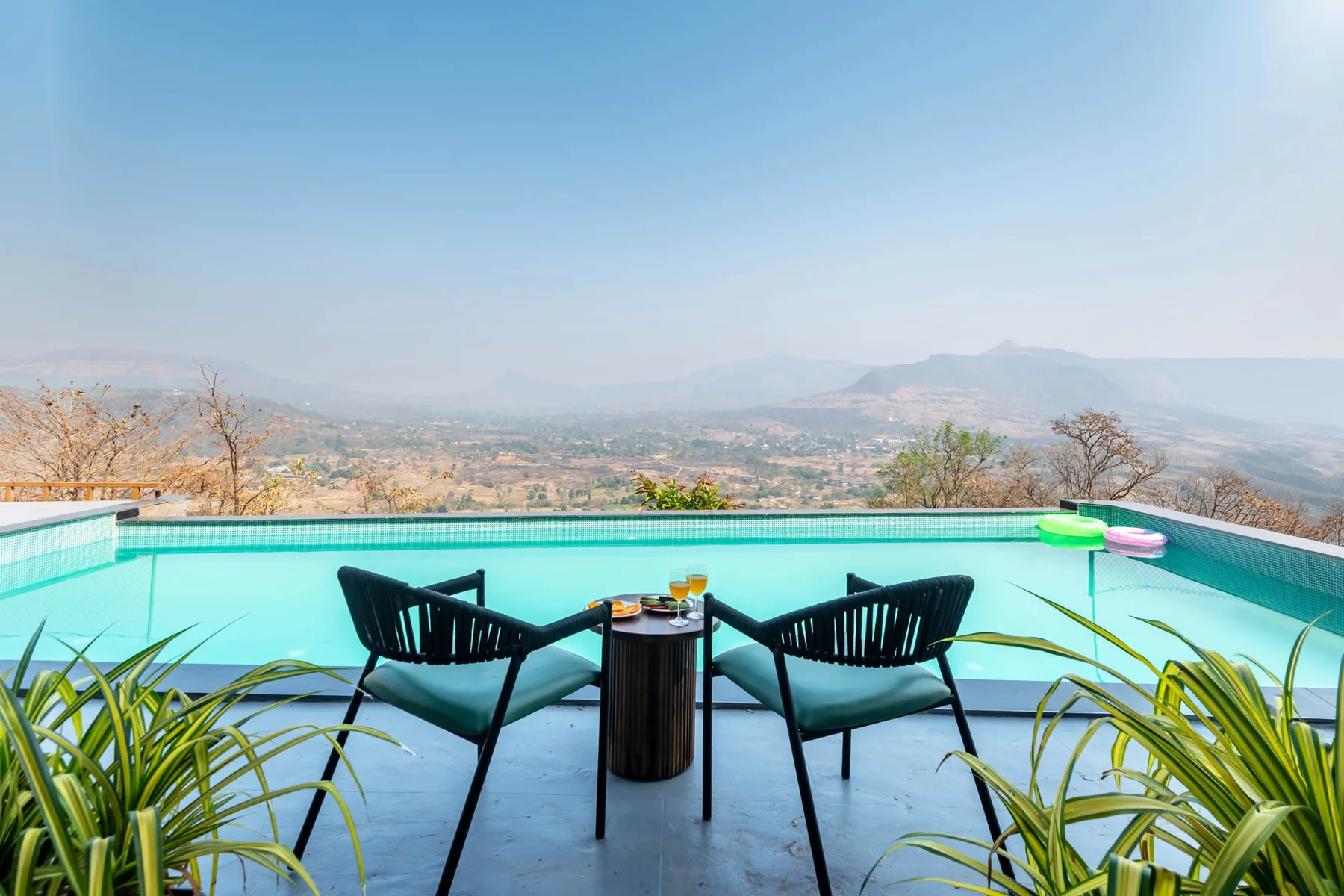 An outdoor poolside seating area overlooks a broad mountain landscape.