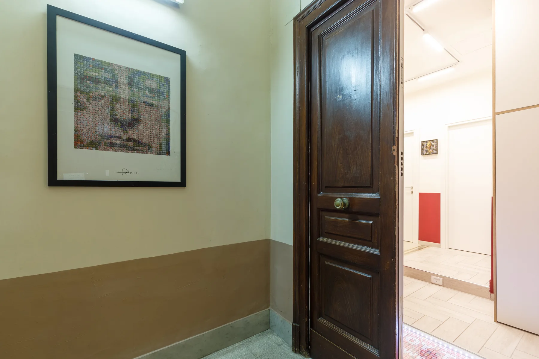 A dark wooden doorway opens into a brightly lit gallery with framed artwork.
