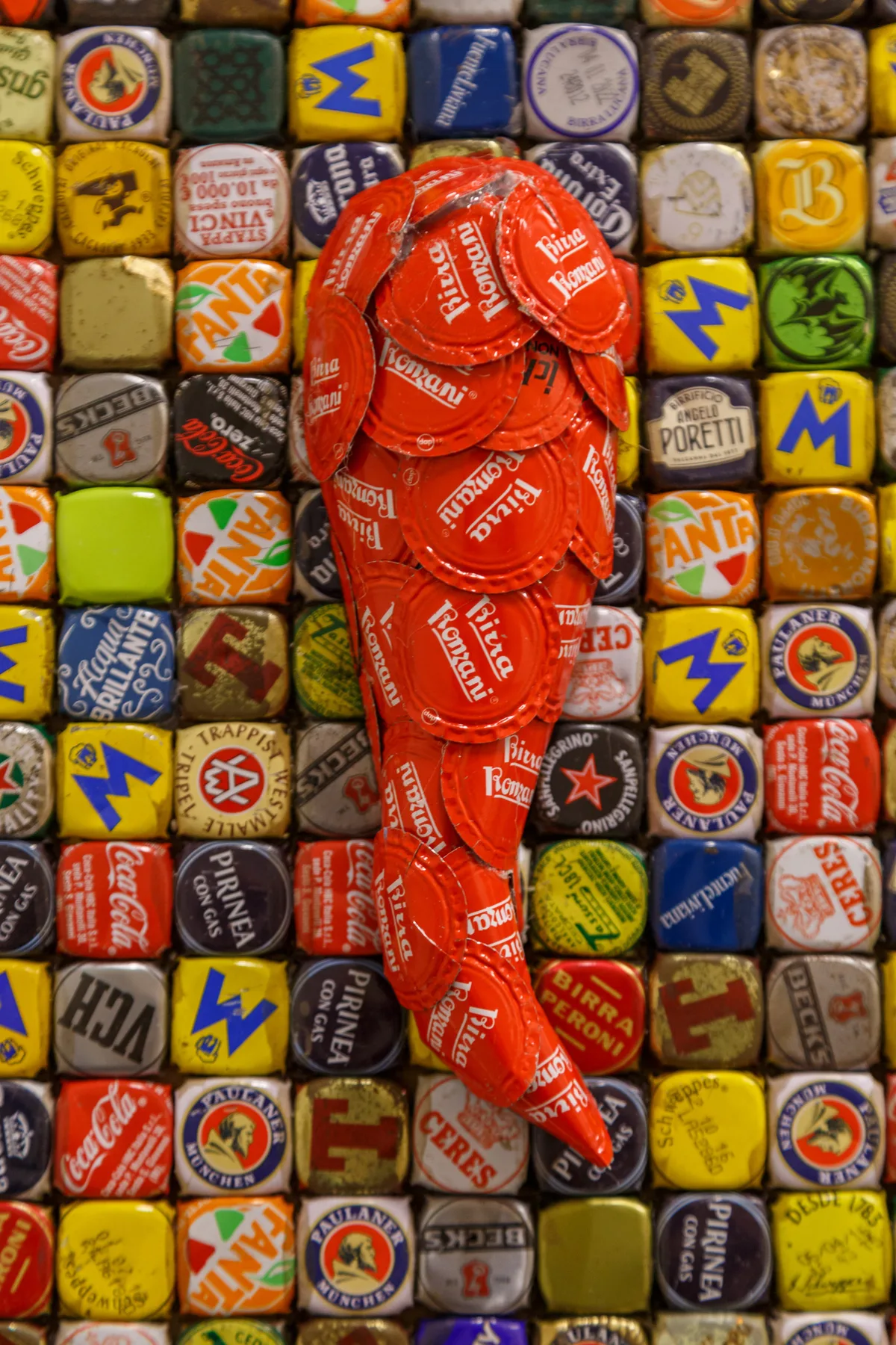 A colorful mosaic of bottle caps surrounds a sculptural arrangement of red caps.