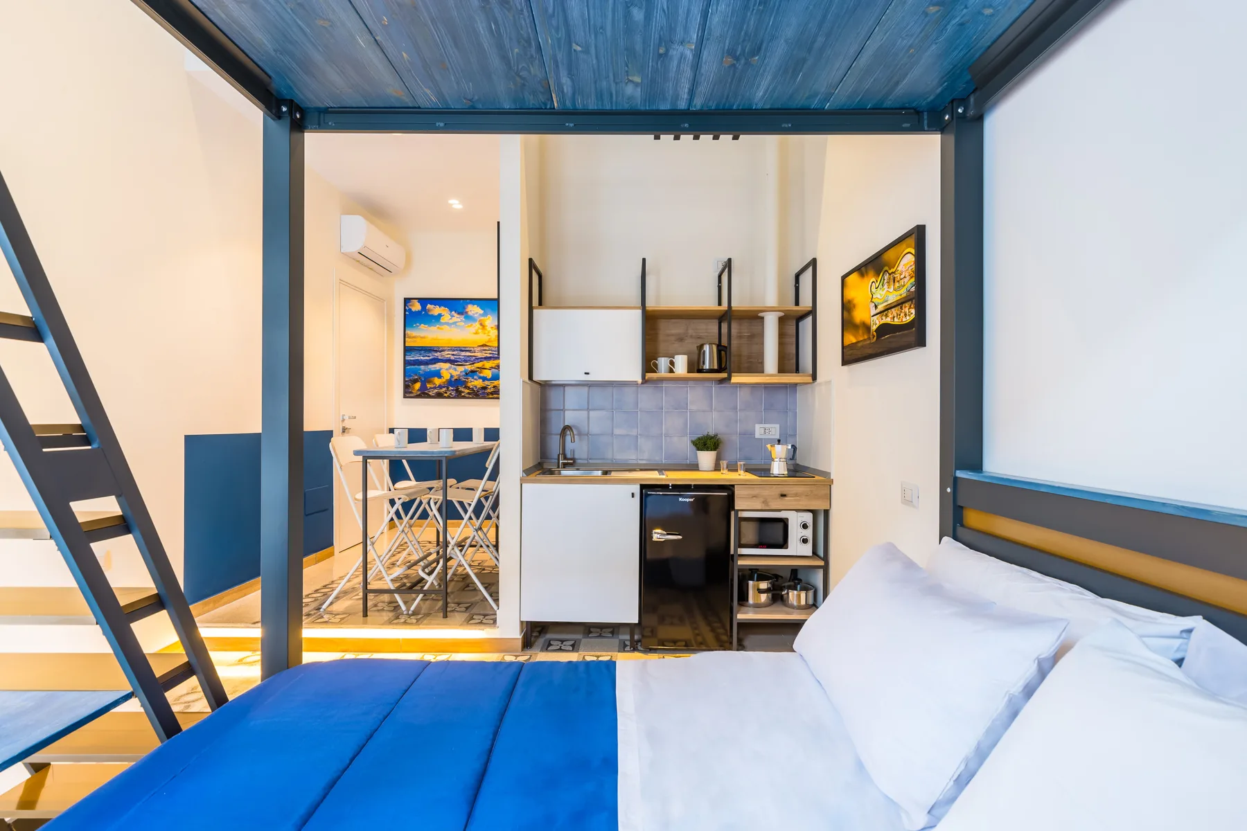 A bedroom with a bed beside a compact kitchenette and dining area.