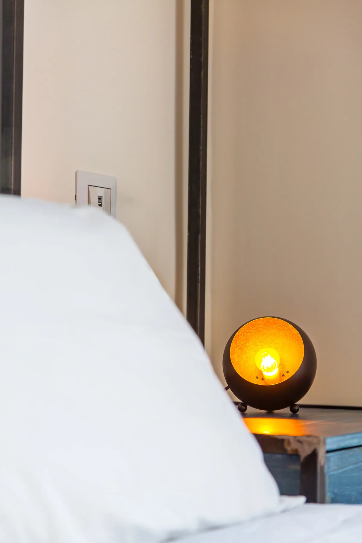 A bedroom scene with white bedding and a glowing bedside lamp.