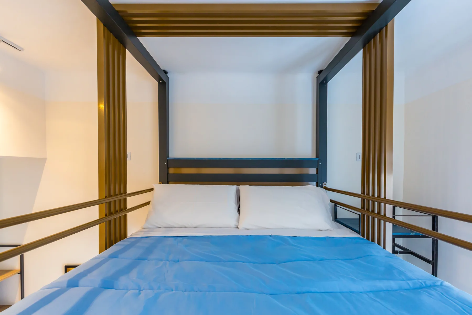 A bedroom with a double bed beneath a dark wood canopy frame.