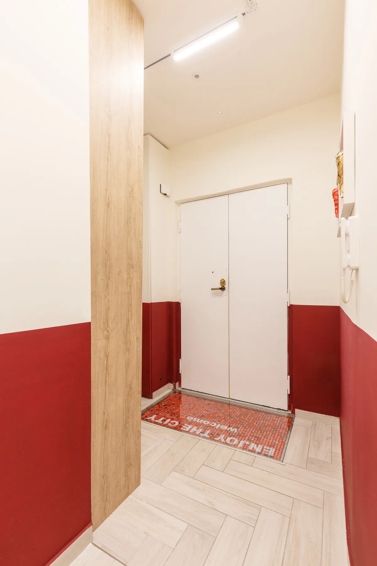 A narrow entryway with a white door, red lower walls, and pale tiled flooring.
