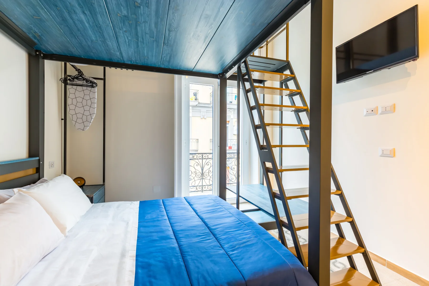 Un dormitorio con ropa de cama azul y una escalera que lleva a una litera superior.