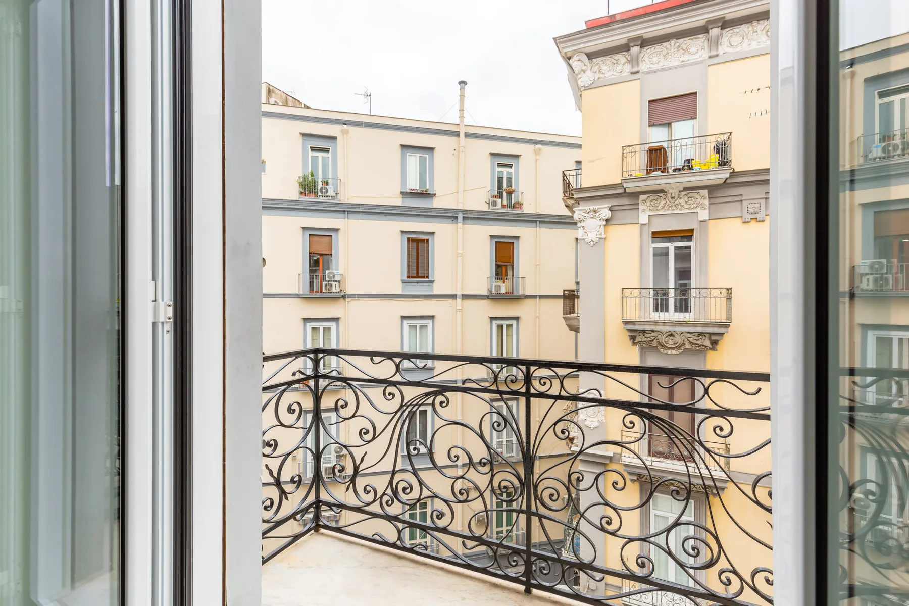 A balcony with an ornate metal railing overlooks neighboring apartment buildings.