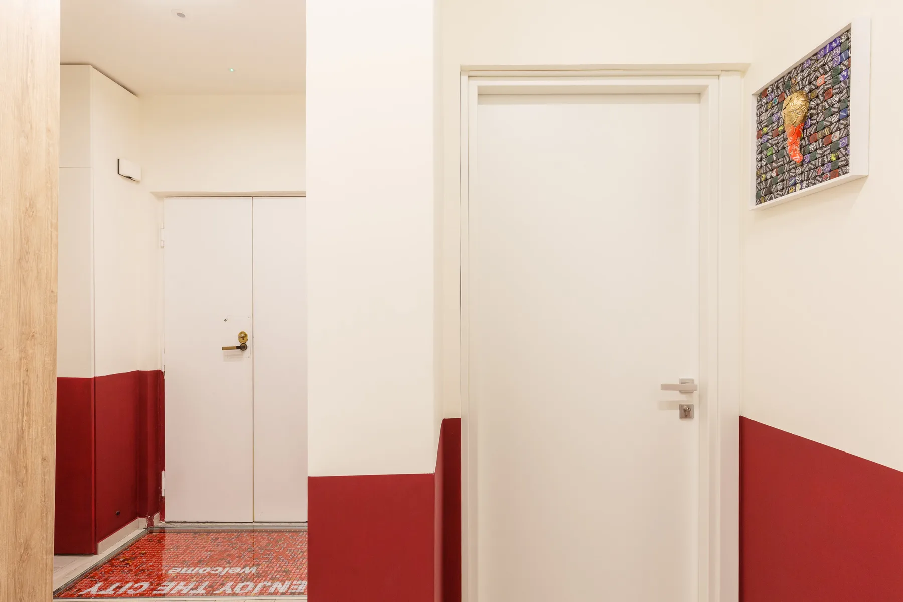 An indoor hallway with white doors, red lower walls, and a patterned floor mat.