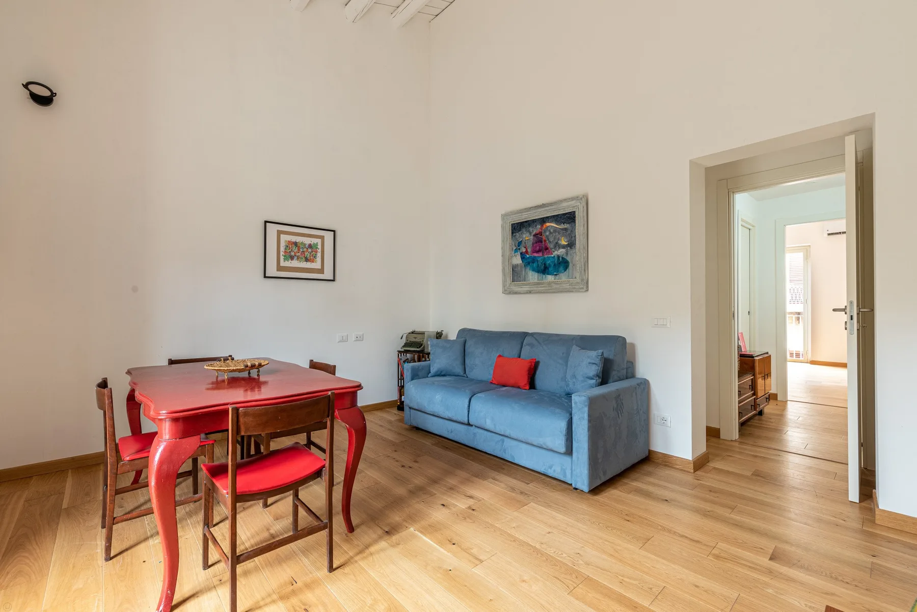 Un salón luminoso con un sofá azul y una mesa de comedor roja.