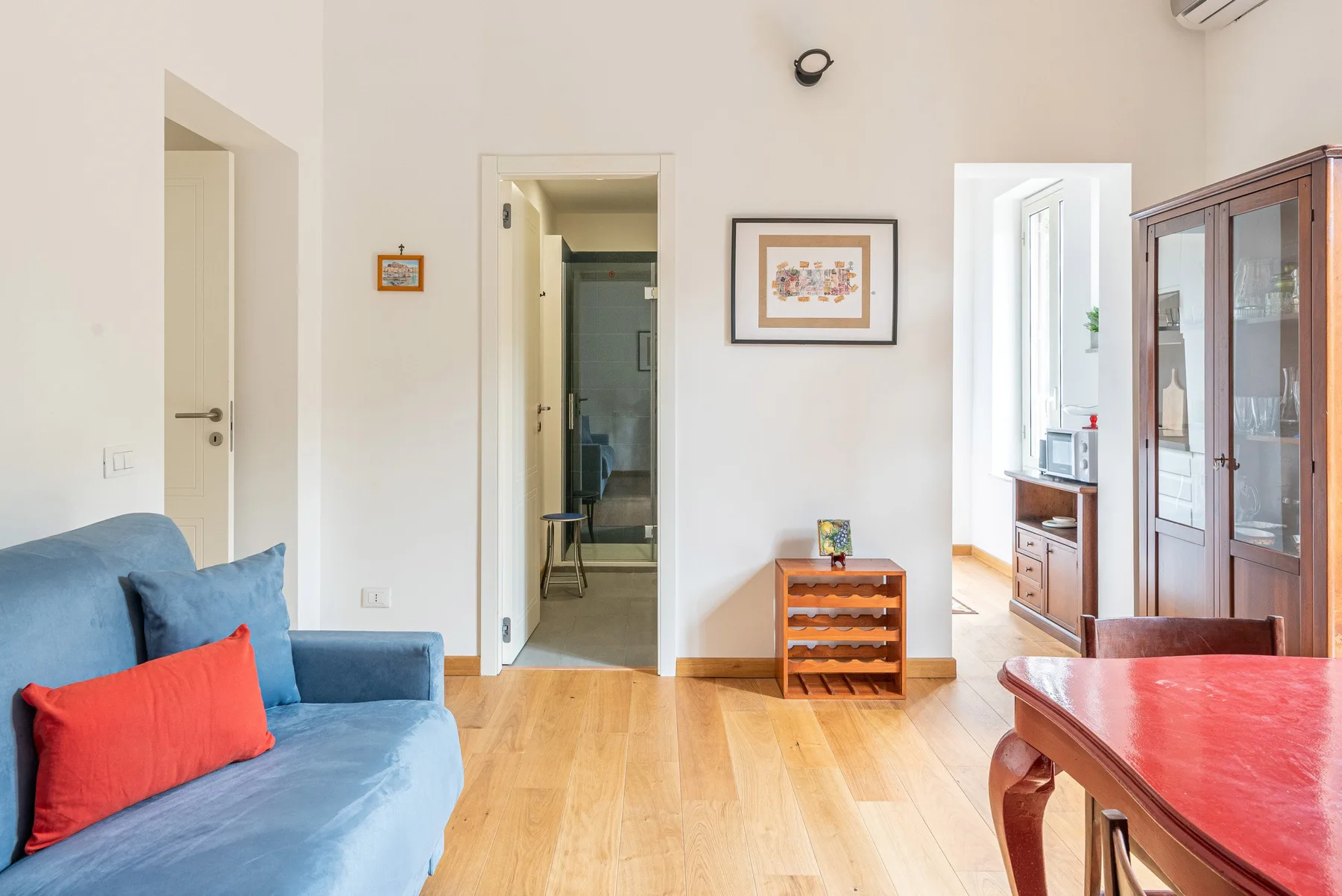 Una sala luminosa con un sofá azul, un mueble de madera y una mesa de comedor.