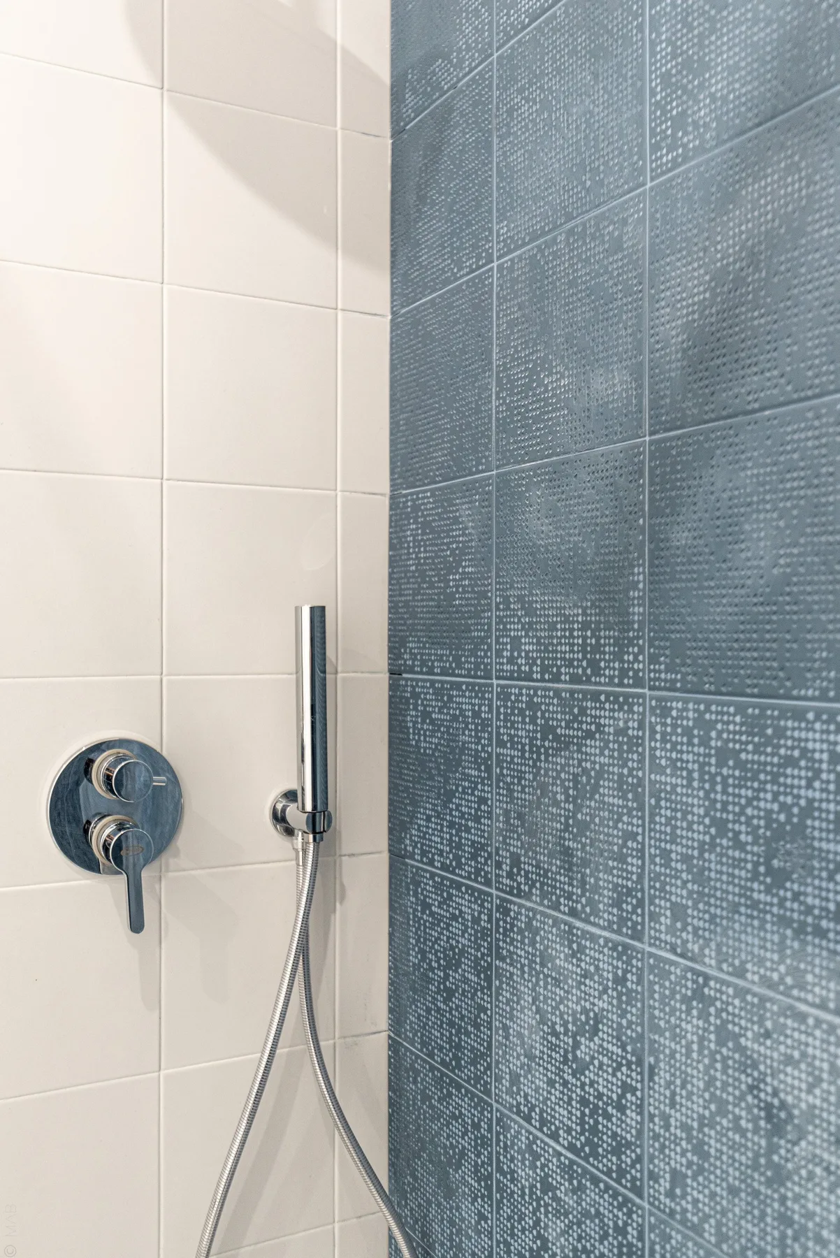 Una zona de ducha con azulejos, una ducha de mano y controles en la pared.