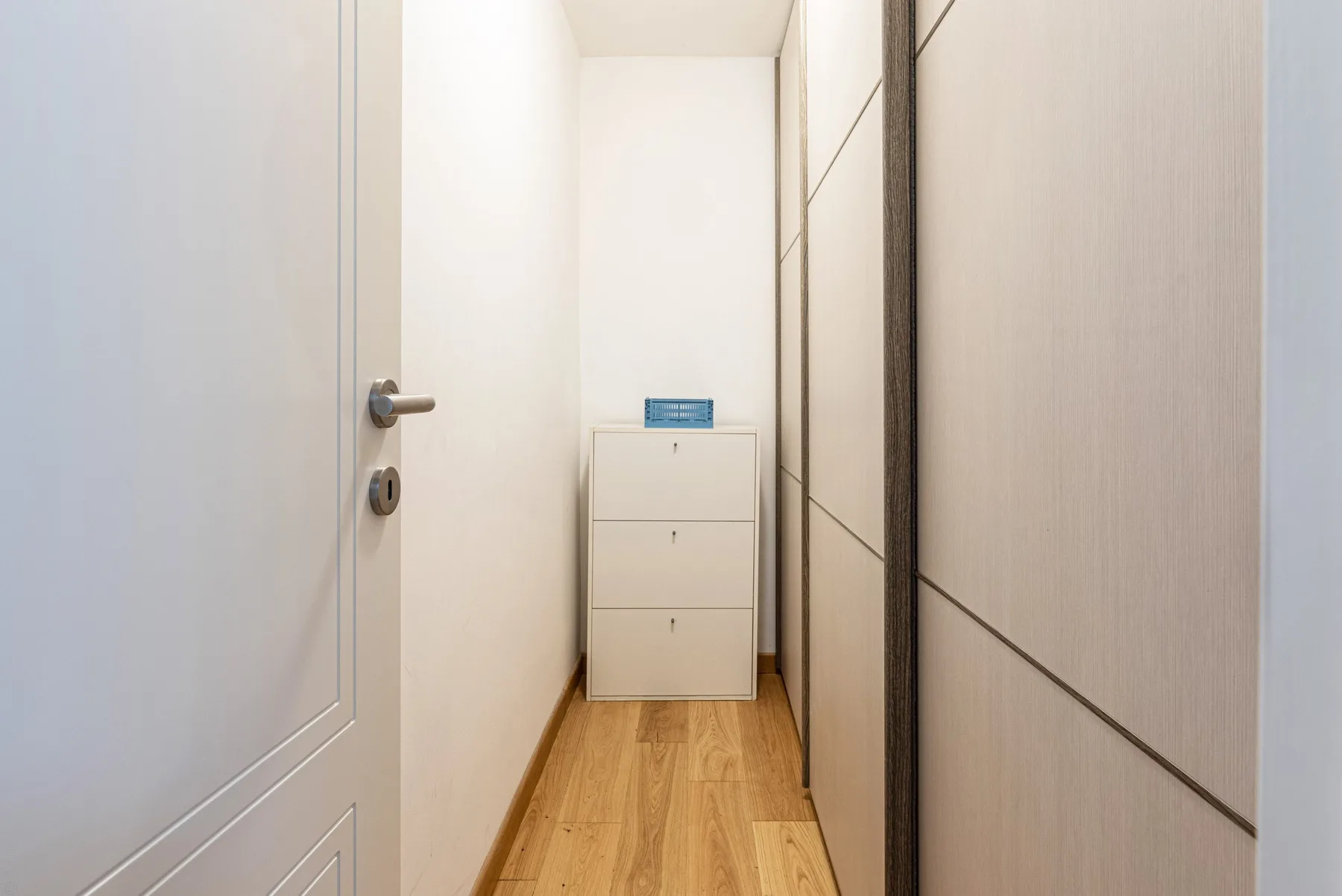Un pasillo estrecho con una puerta blanca y armarios empotrados.