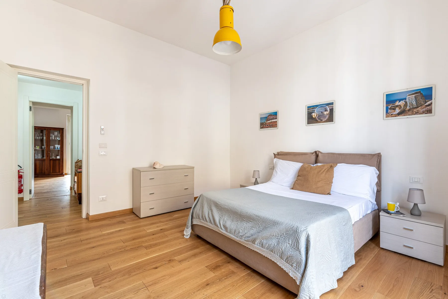 Un dormitorio luminoso con una cama doble, una cómoda y cuadros en la pared.