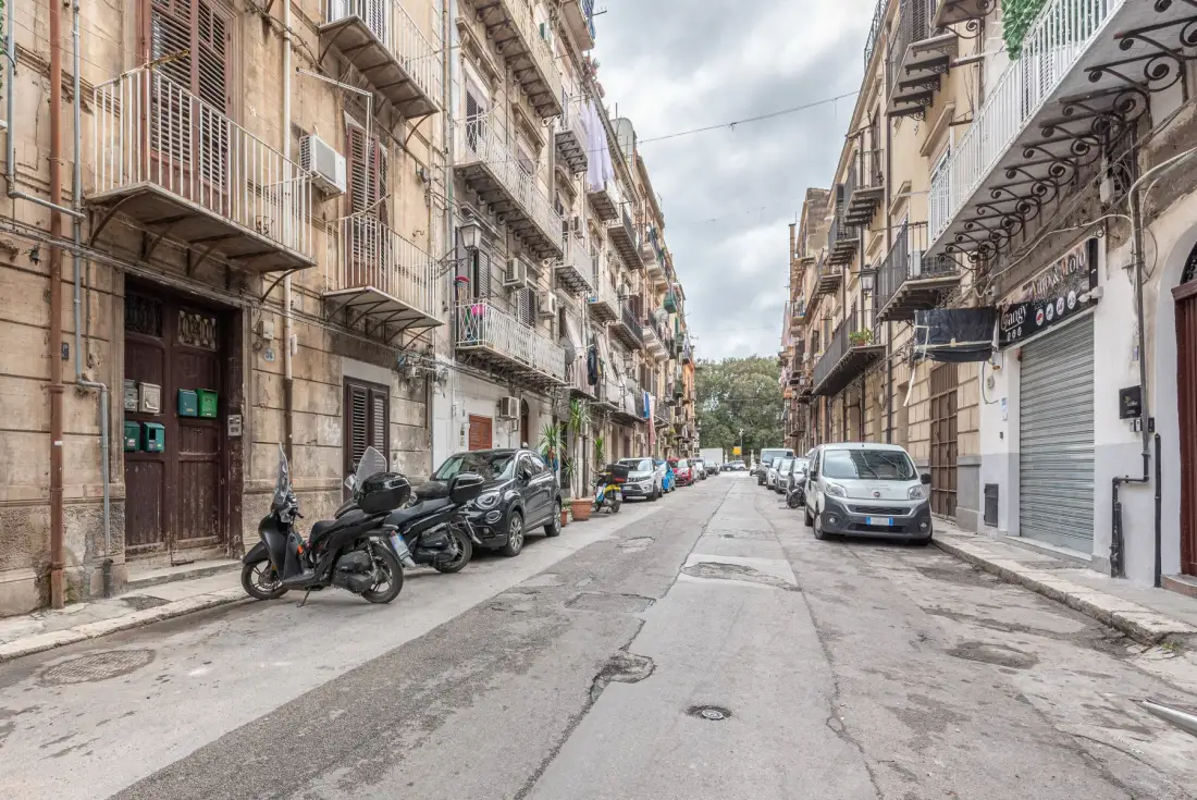 Una calle urbana estrecha, flanqueada por edificios contiguos y vehículos estacionados.