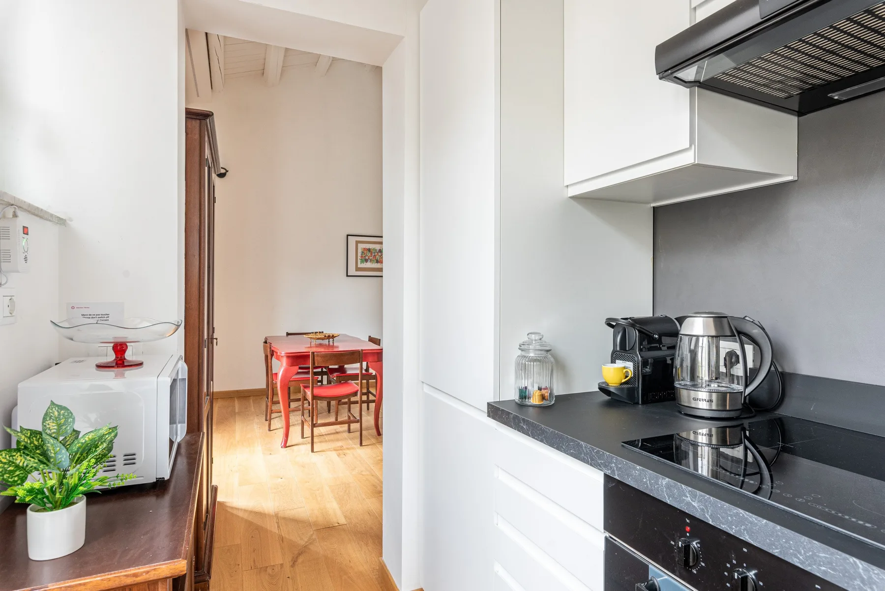 Una cocina compacta con cafetera y hervidor sobre la encimera, junto a un comedor abierto.