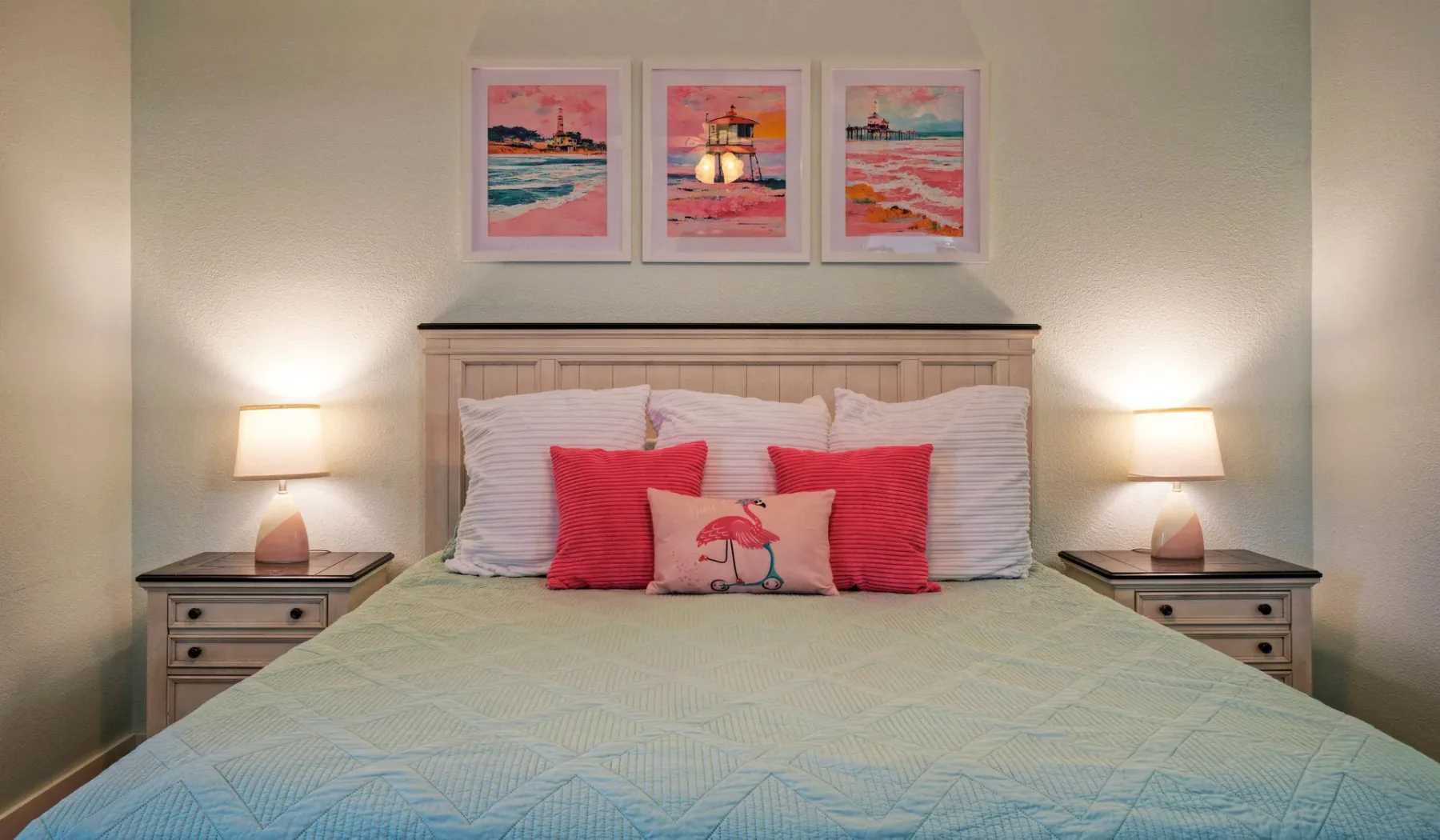 Una cama bien tendida con almohadas coloridas está bajo tres cuadros.