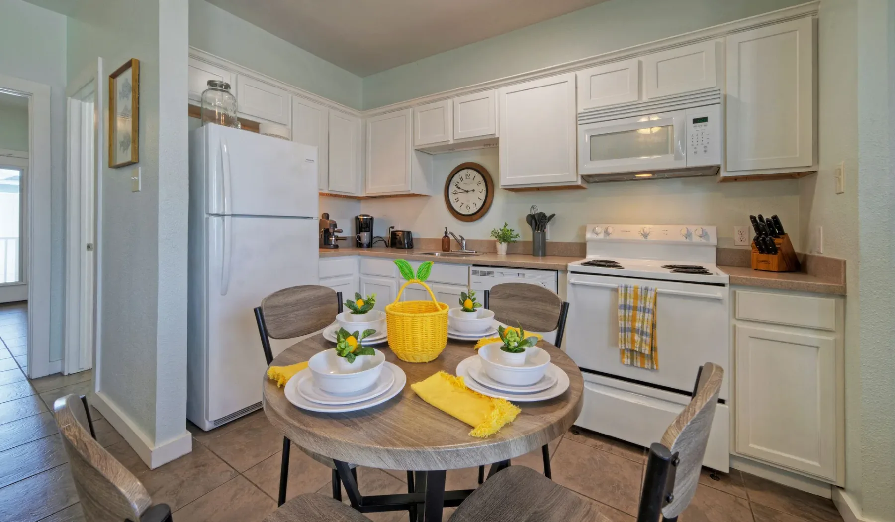 Una cocina con zona de comedor, armarios blancos y una mesa puesta.