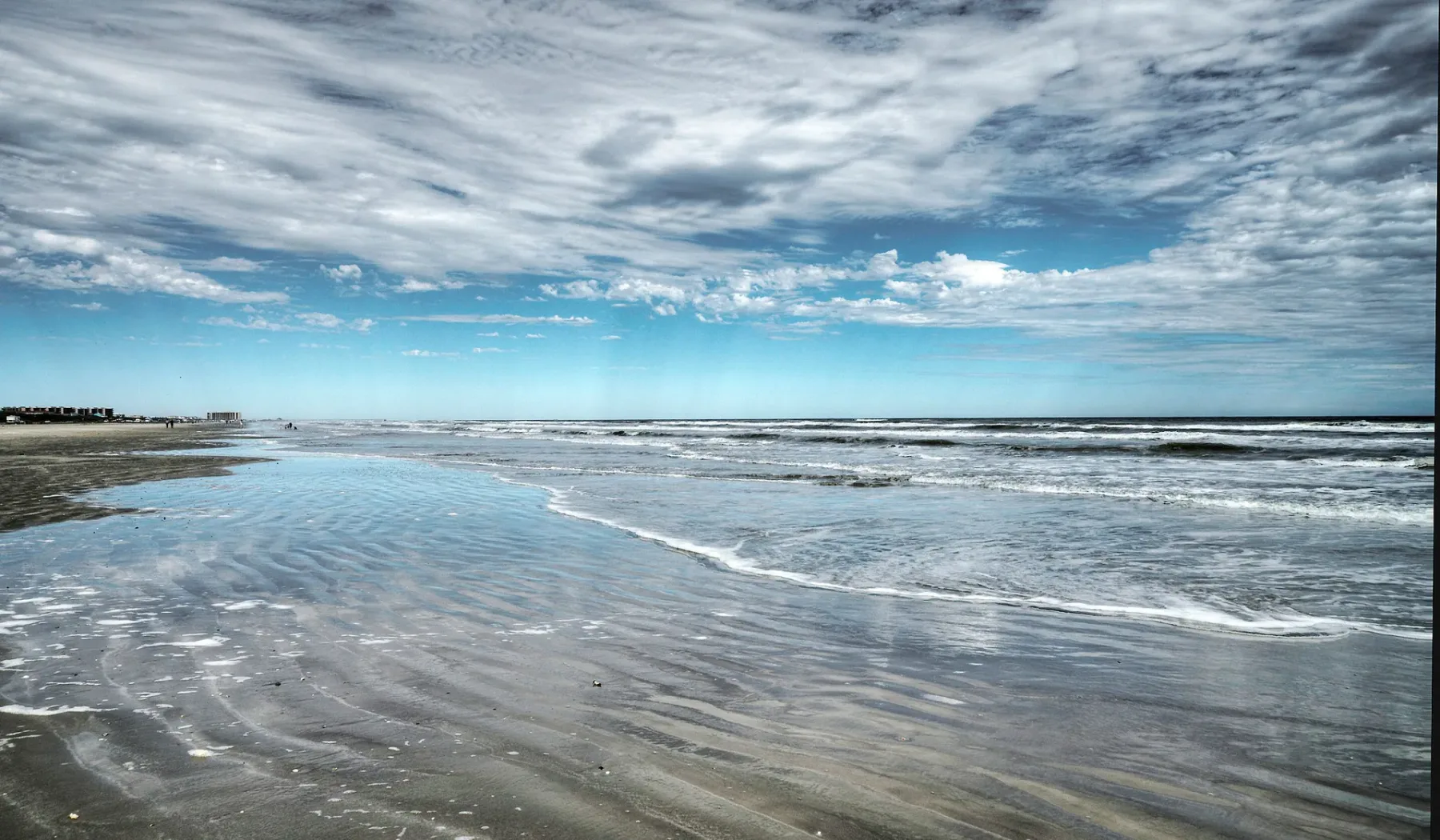 Una costa de playa con olas poco profundas bajo un cielo nublado.