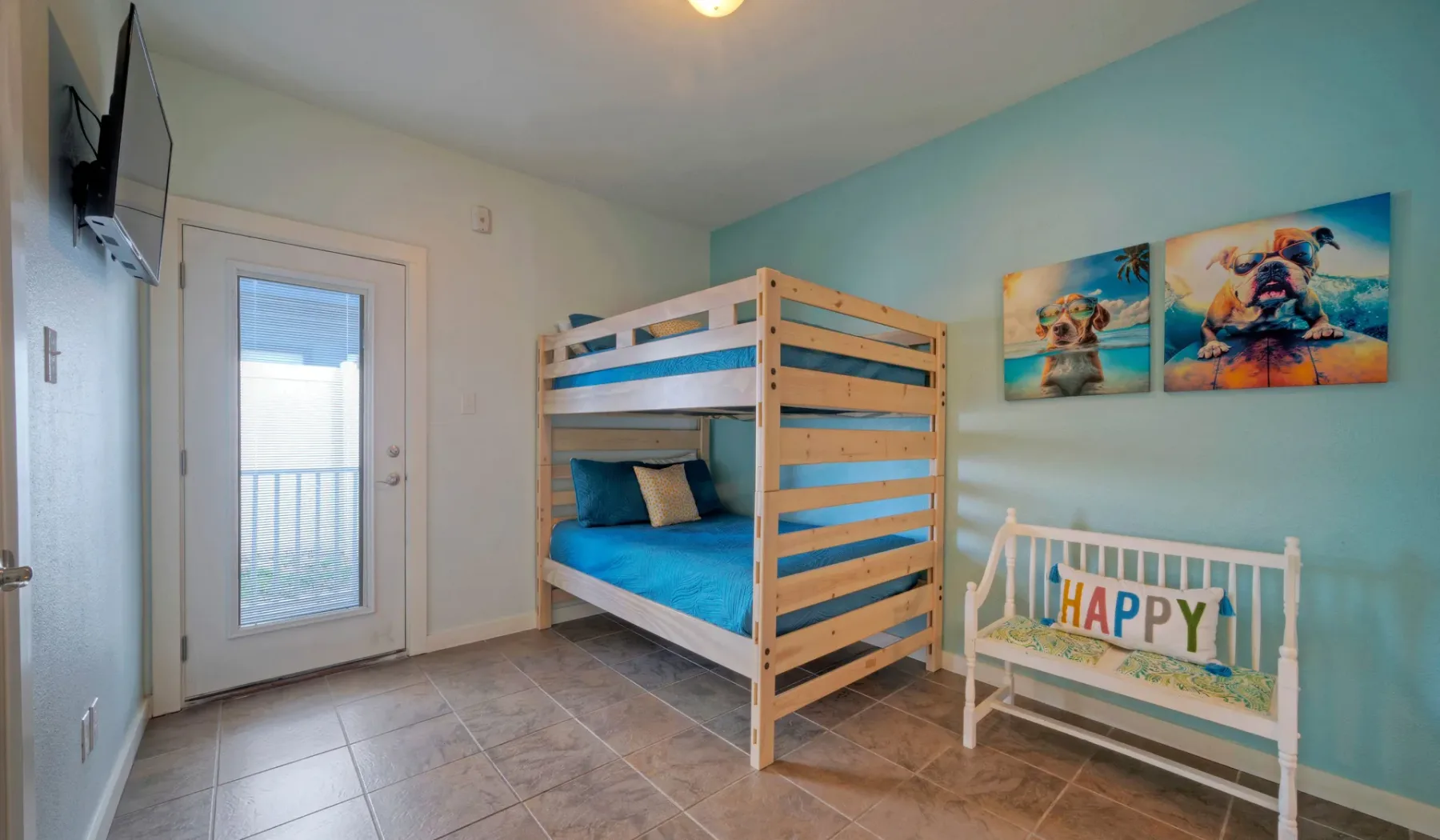 Un dormitorio con litera, ropa de cama azul, cuadros coloridos y un banco pequeño.