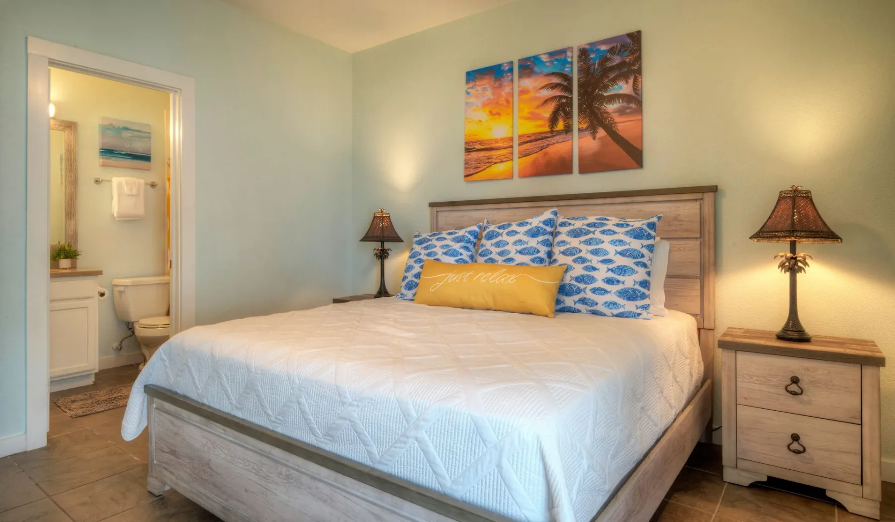 Un dormitorio con una cama bien arreglada y una colorida escena de playa sobre el cabecero.