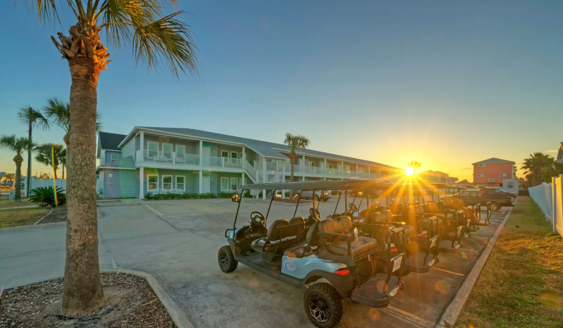 Una fila de carritos de golf está junto a un edificio de dos pisos al atardecer.