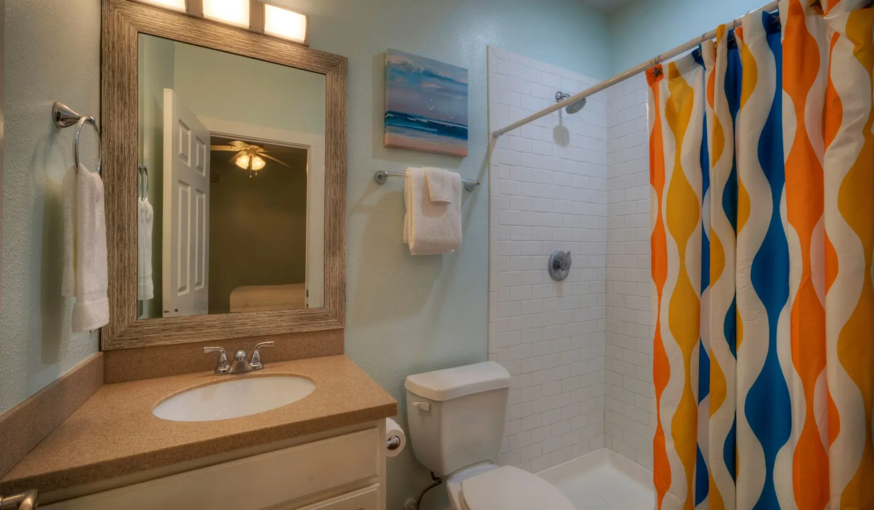 Un baño con lavabo, espejo, inodoro y cortina de ducha colorida.