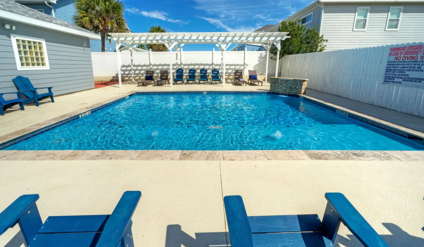 Una piscina al aire libre está rodeada de asientos azules y una pérgola blanca.