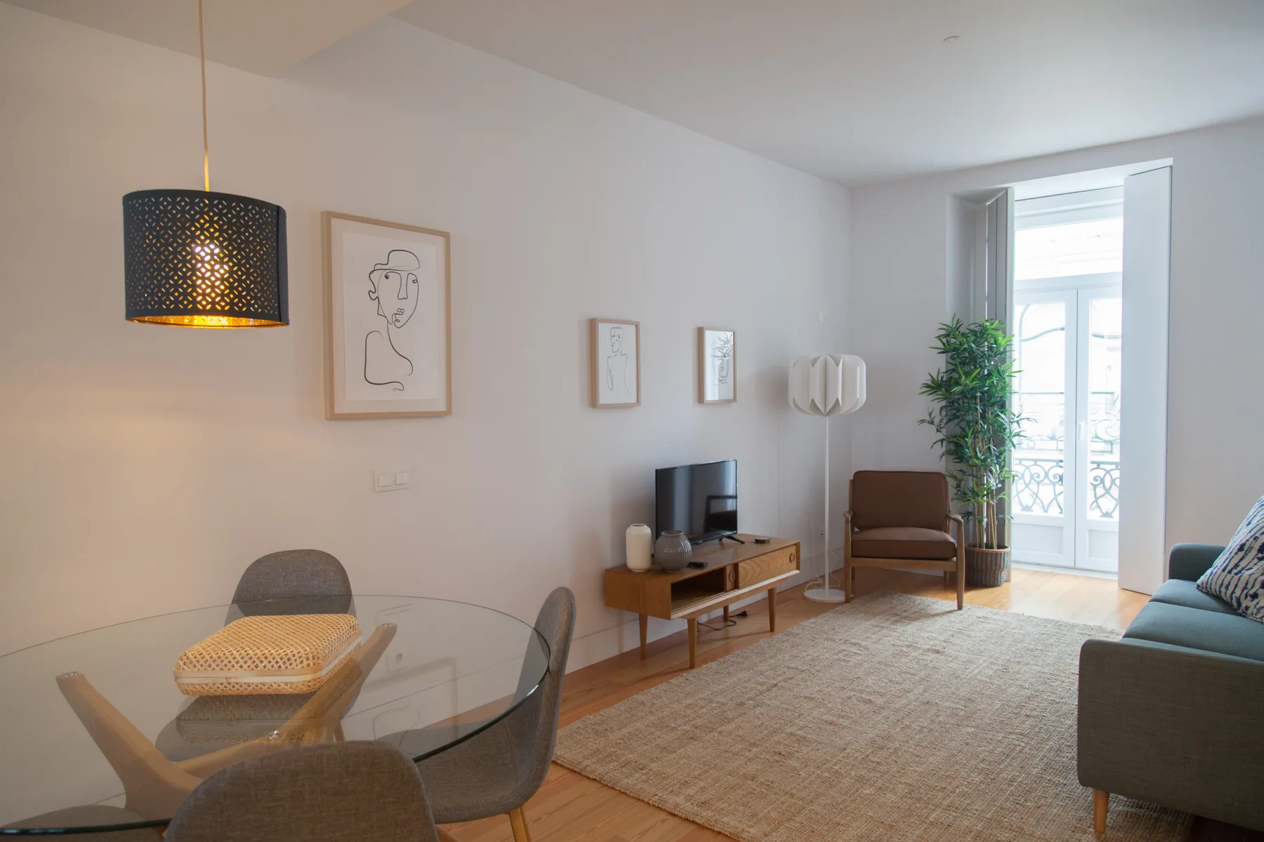 Una sala luminosa con asientos, un televisor y una puerta abierta al balcón.