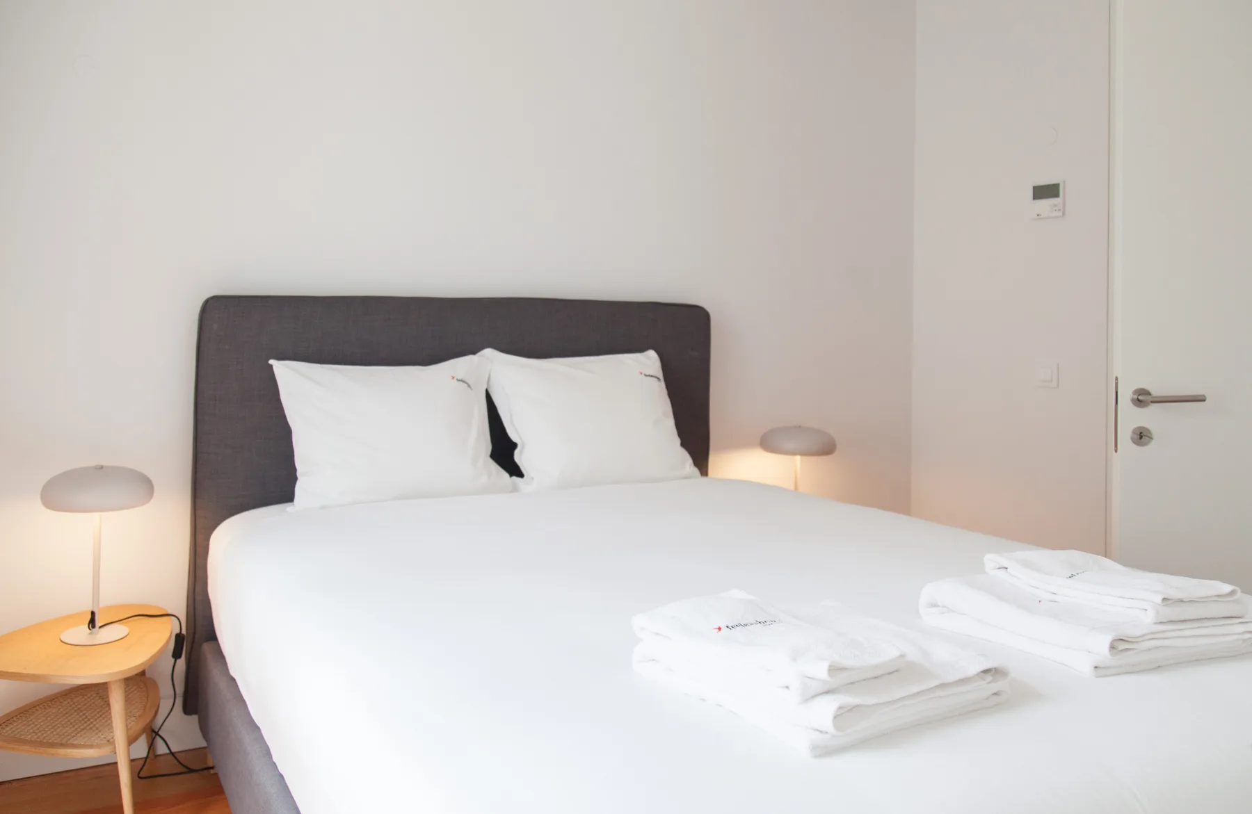 Un dormitorio con una cama, ropa de cama blanca y lámparas de noche.