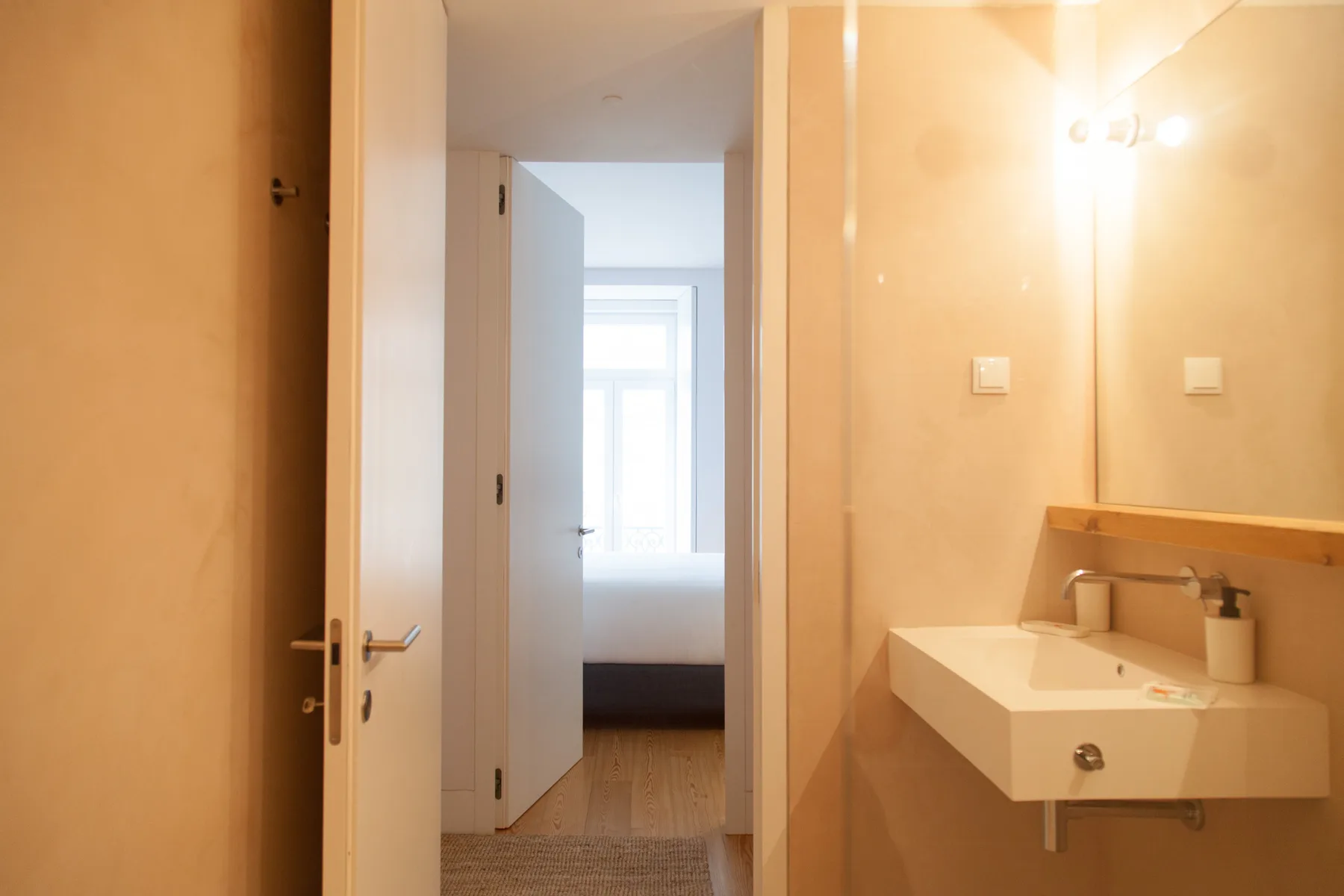 Un lavabo de baño está junto a una puerta abierta que da a una habitación luminosa.