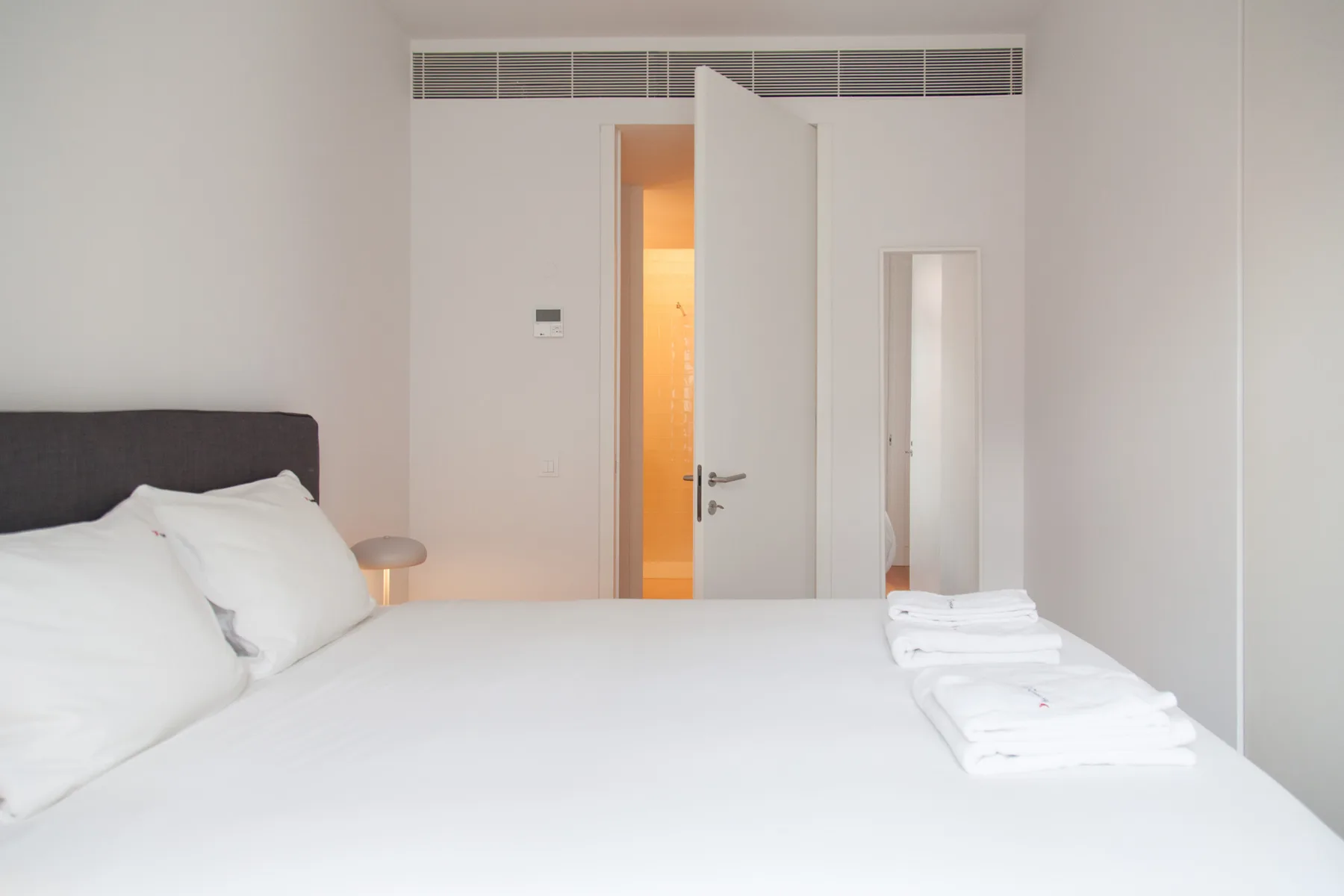 Un dormitorio luminoso con ropa de cama blanca y una puerta abierta.