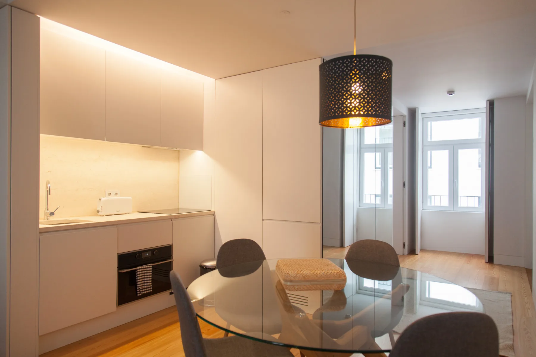 Cocina y comedor modernos con armarios claros y una mesa de vidrio.