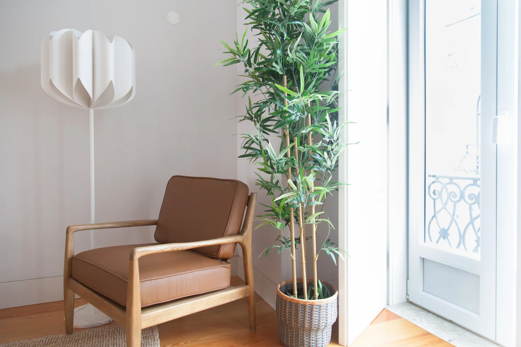 Una luminosa zona de estar con un sillón marrón, una lámpara de pie y una planta en maceta.