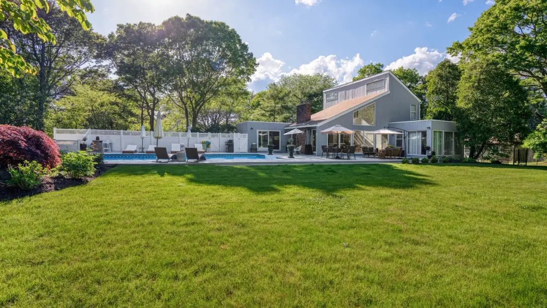 A modern house and swimming pool sit beyond a broad green lawn.