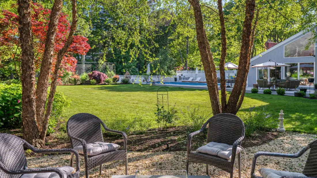 A leafy garden with outdoor seating, a lawn, and a swimming pool.