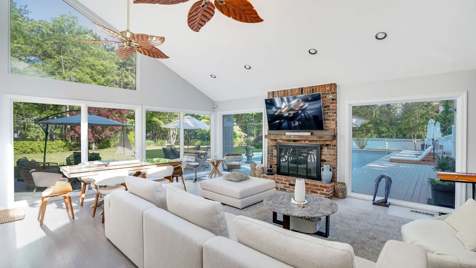 A bright living room with seating around a fireplace and views of a pool.