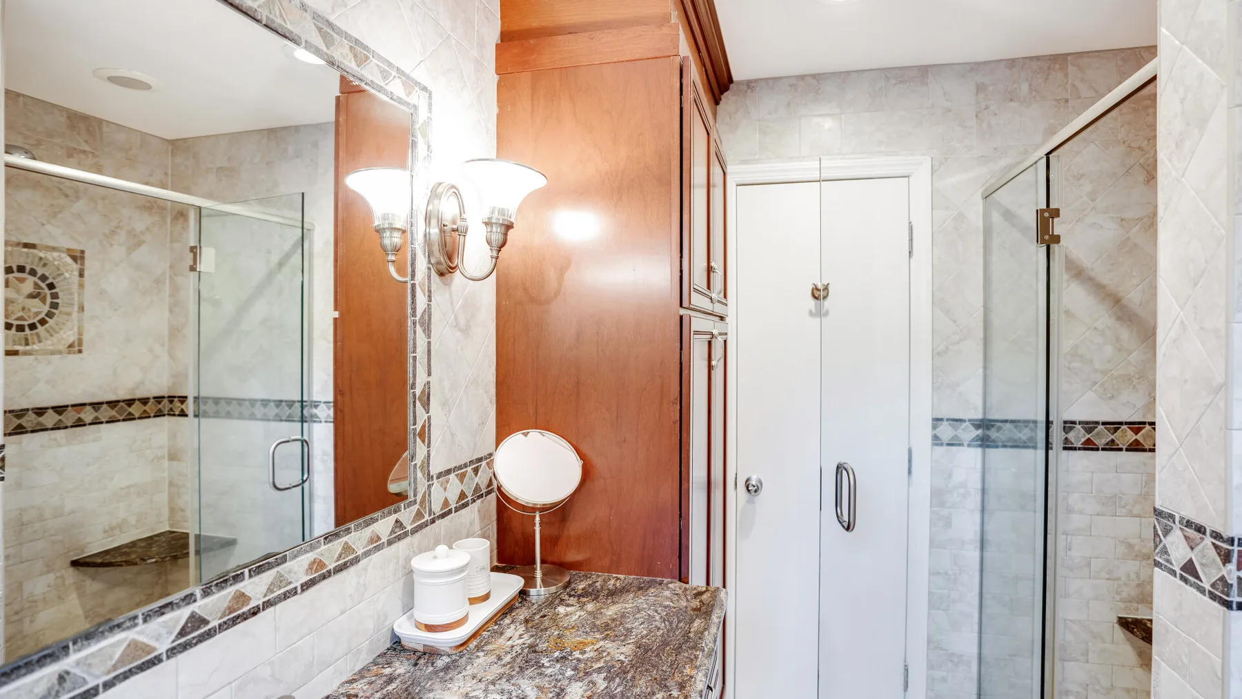 A tiled bathroom with a glass shower and a mirrored vanity.